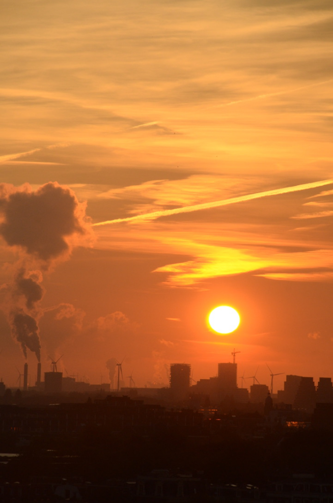 Power plants and wind turbines under condensation trails at sunset (view from hotel window during the 2024 EASST-4S Conference in Amsterdam). Photograph by Eva Gray.